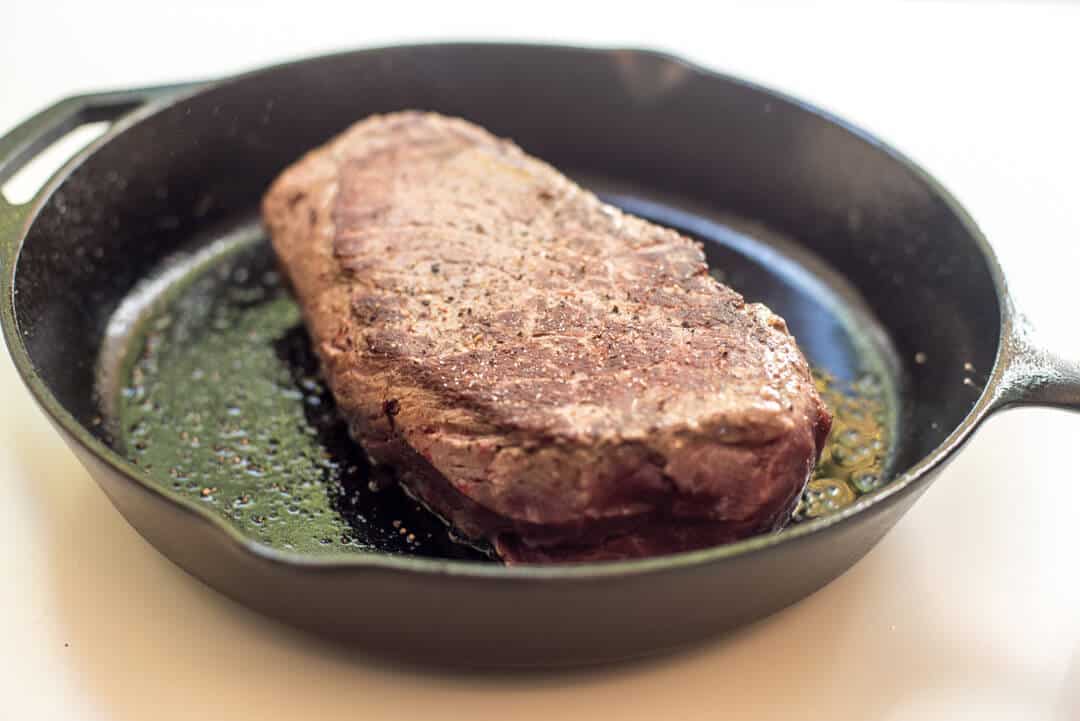 A pot roast cooking in a cast iron skillet.