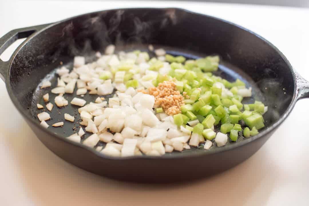 Onion, celery, and garlic cooking in a cast iron skillet.