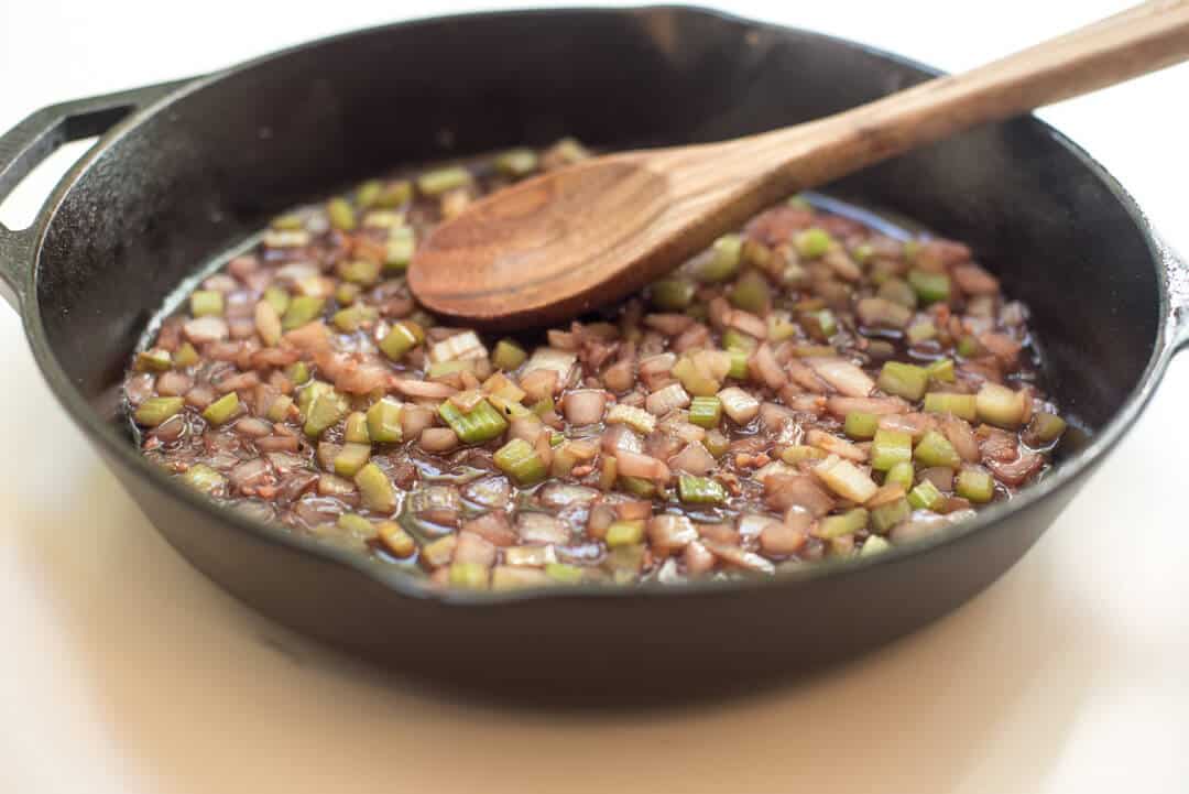 A mixture of onion and celery with red wine in a cast iron skillet with a wooden spoon.