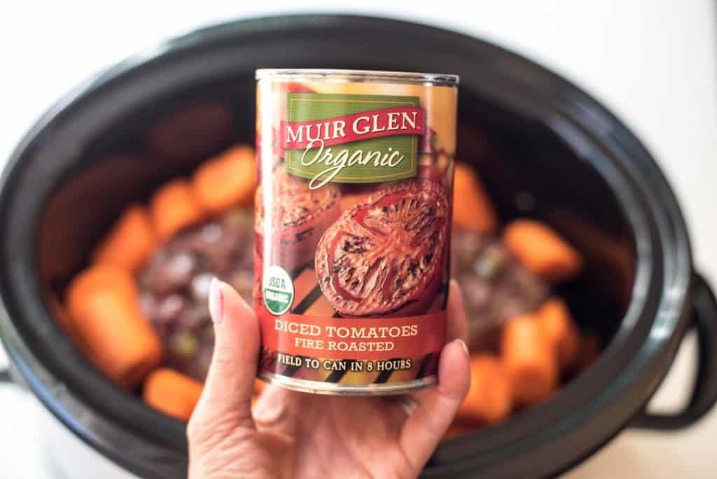 A hand holding a can of Muir Glen Organic Fired Roasted Diced Tomatoes.