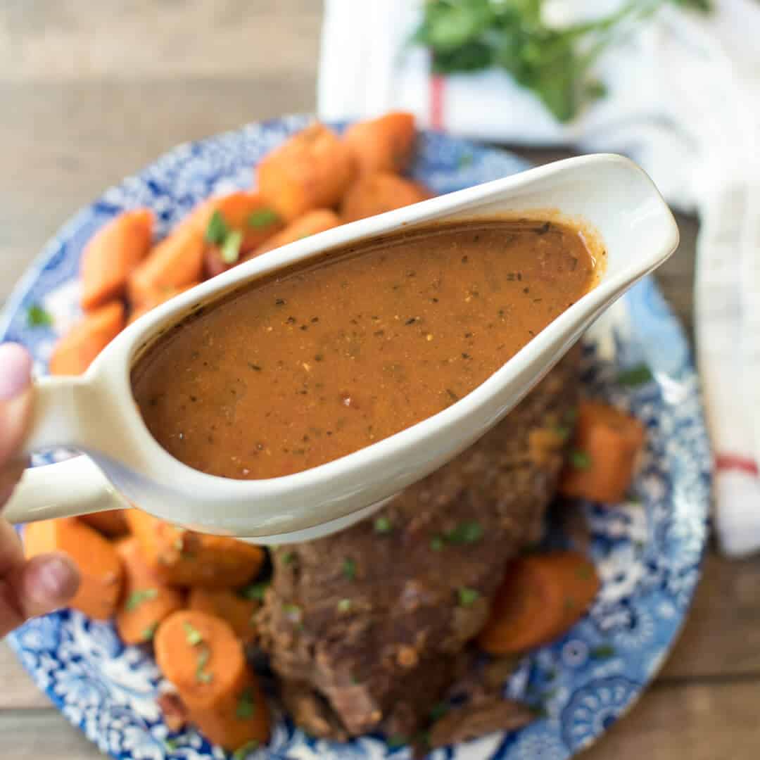 A hand holds a gravy boat filled with gravy.