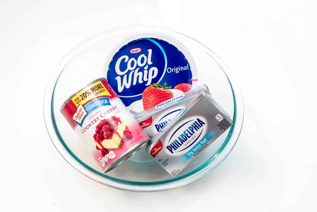 Comstock Country Cherry Pie Filling, Cool Whip, and Philadelphia Cream Cheese in a glass bowl.