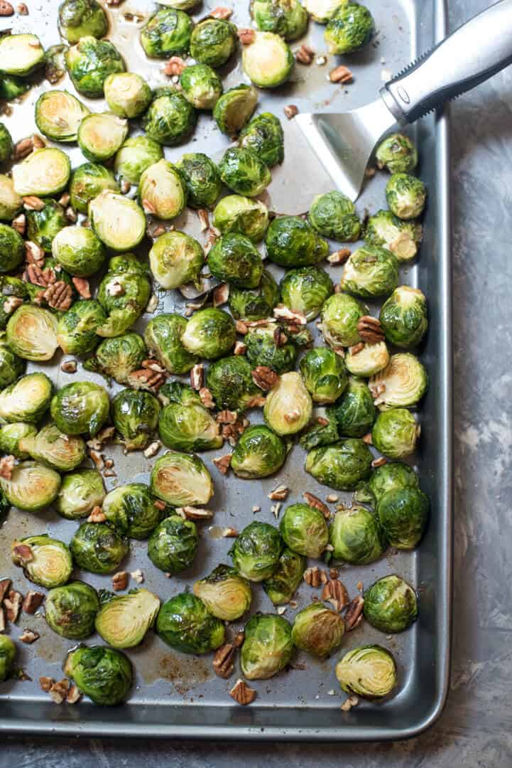 A spatula scoops brussels sprouts from a baking sheet.