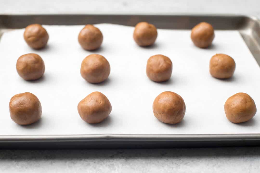 Balls of cookie dough on a parchment paper lined baking sheet.