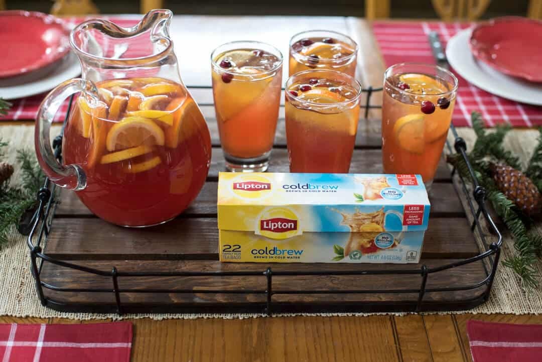 Lipton Cold Brew Tea Bags on a wood tray with glasses and a pitcher of Cranberry Citrus Iced Tea.