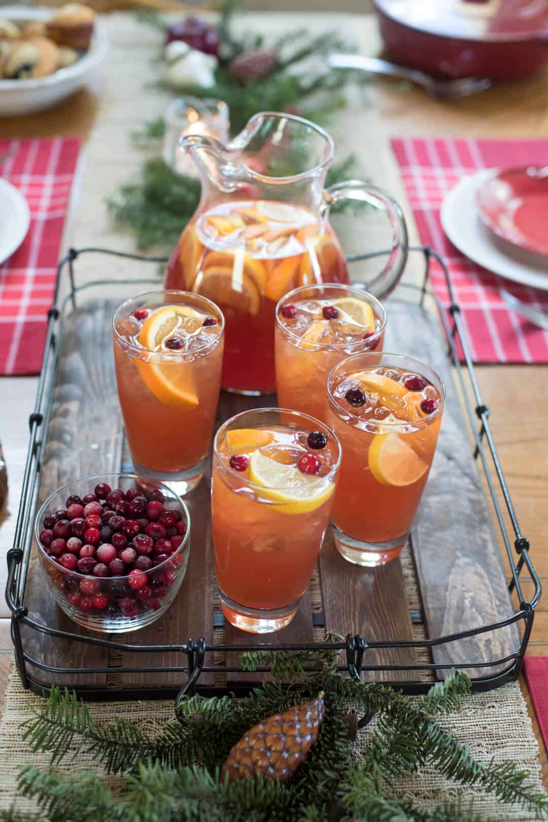 Glasses and a pitcher of iced tea on a wooden tray on a table with Christmas decorations.