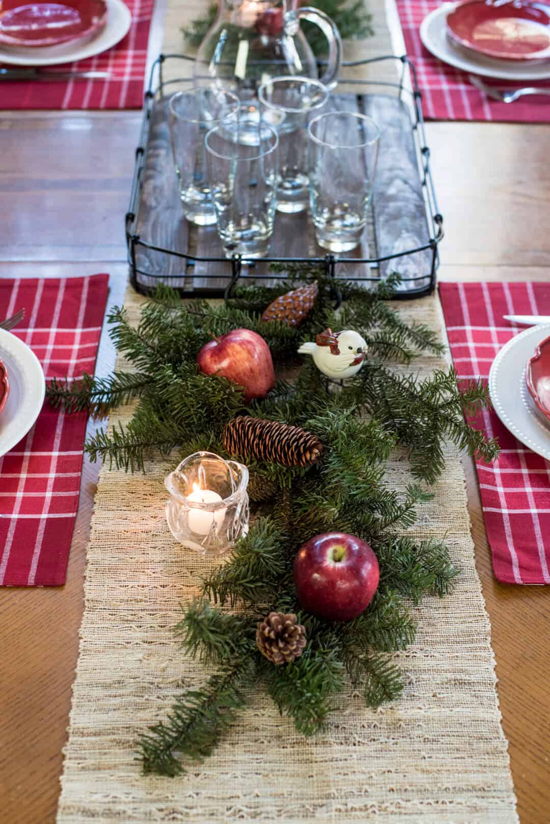 A pretty holiday tablescape with pine branches, pine cones, apples, birds, and candles.