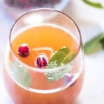 A close up of a glass of cranberry peach prosecco punch topped with cranberries and mint.