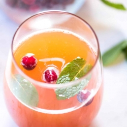 A close up of a glass of cranberry peach prosecco punch topped with cranberries and mint.