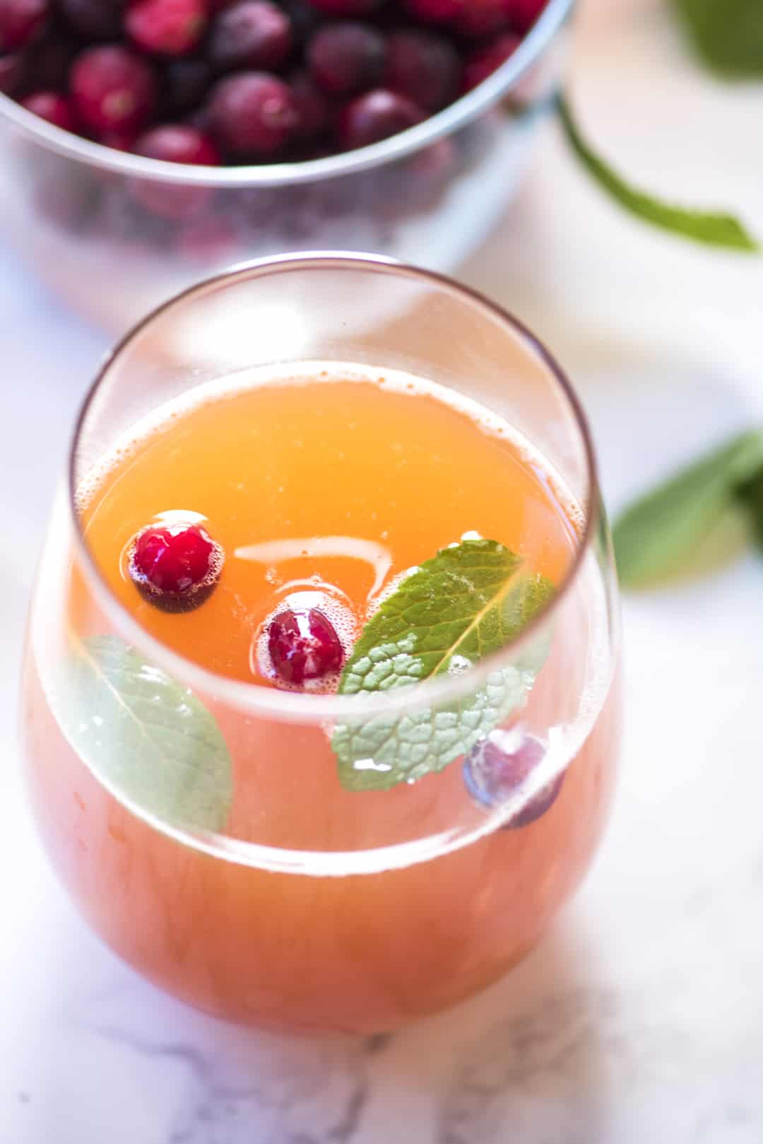 Cranberry Peach Prosecco Punch in a stemless glass topped with fresh cranberries and mint.