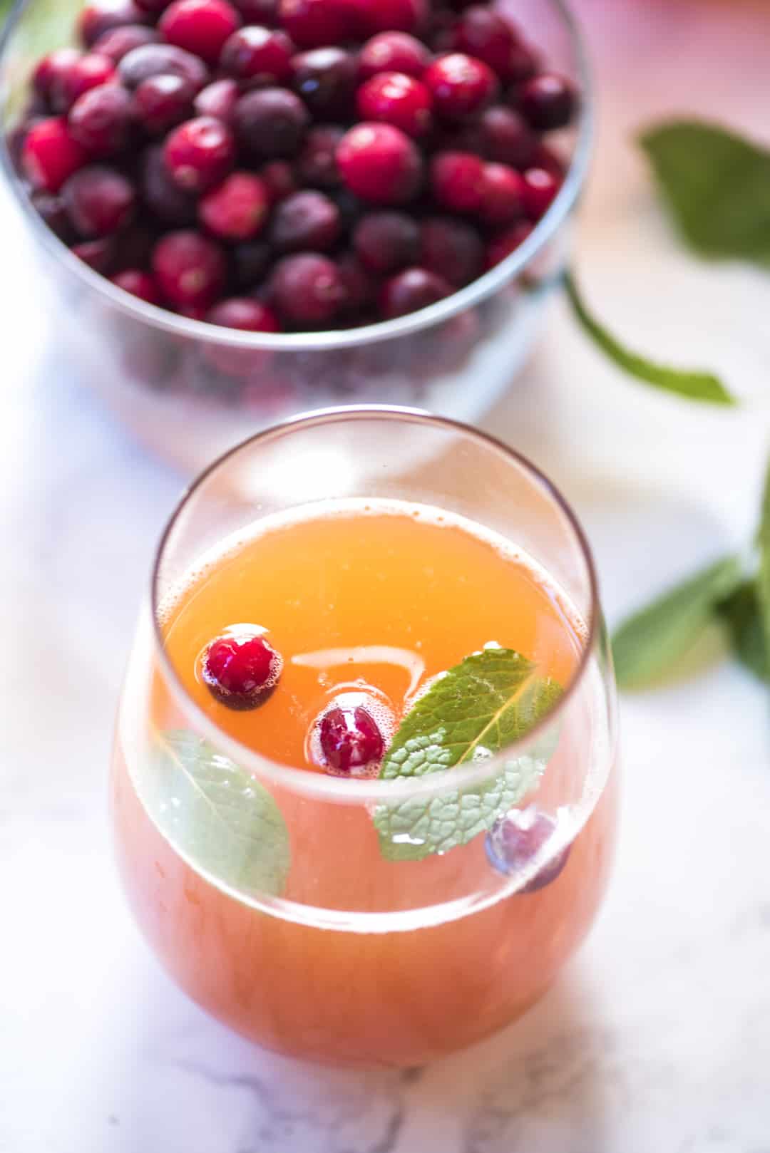 Cranberry Peach Prosecco Punch in a stemless glass topped with fresh cranberries and mint.
