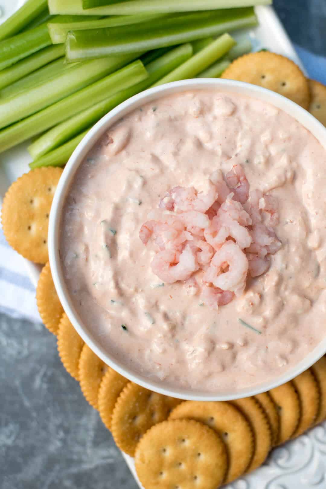 Shrimp Dip in a white bowl on a platter with Ritz crackers and celery.