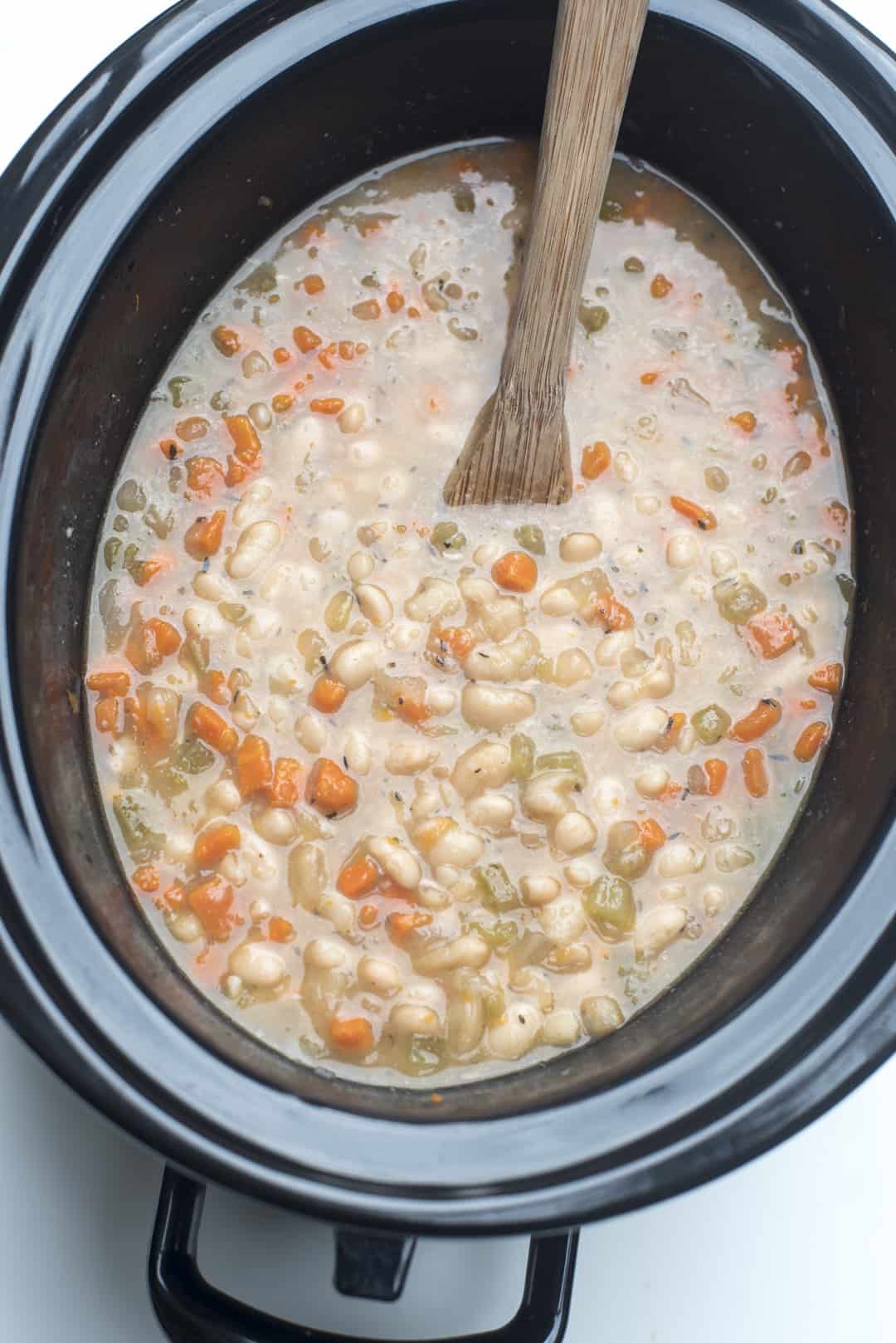A wooden spoon stirs the soup in the slow cooker.