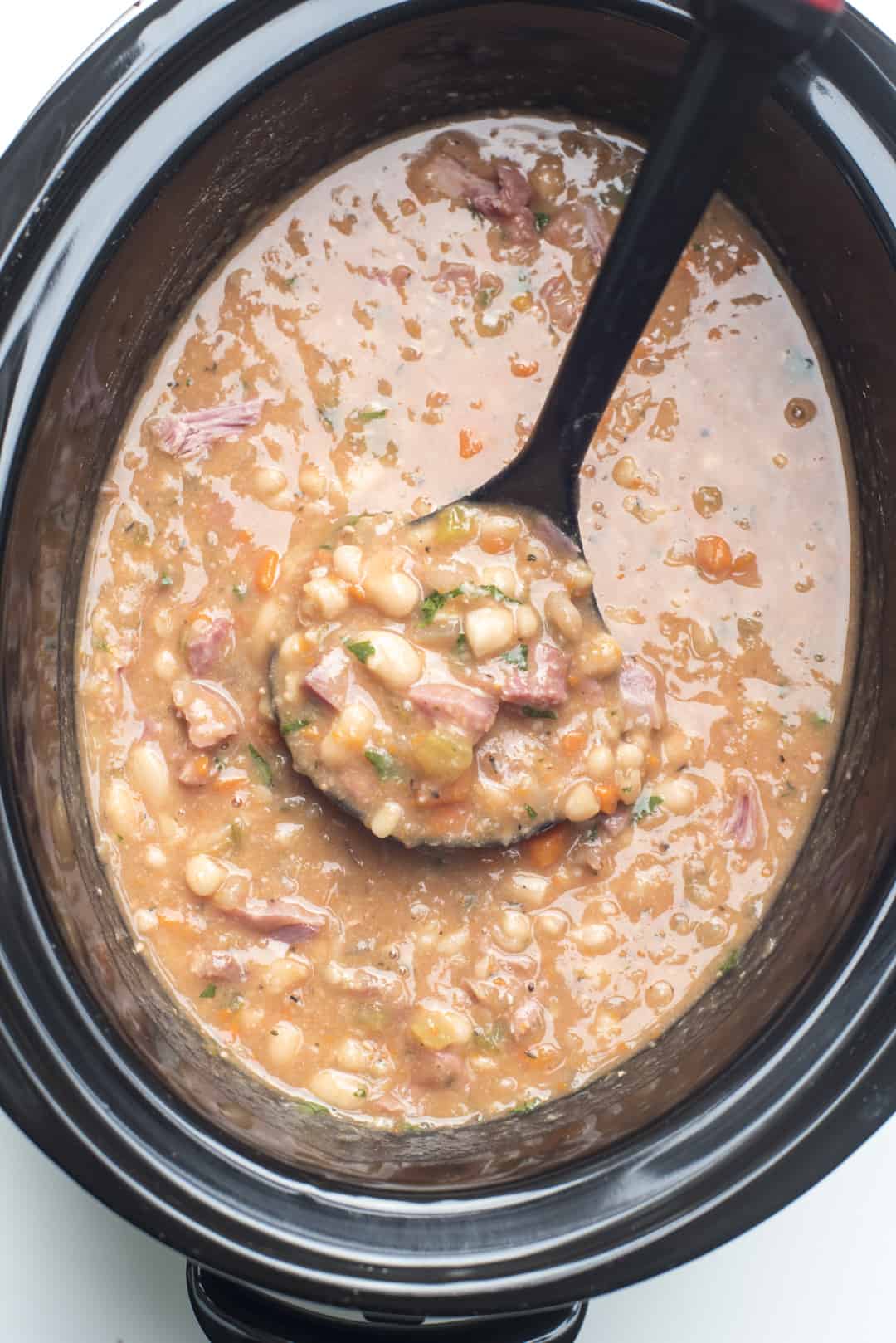Ham and Bean Soup on a slow cooker with a ladle shot from over the top.