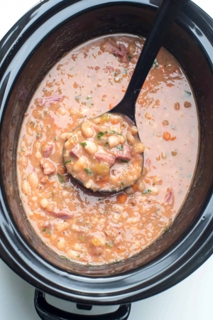 A ladle scoops ham and bean soup from a slow cooker.
