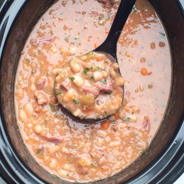 A ladle scoops ham and bean soup from a slow cooker.