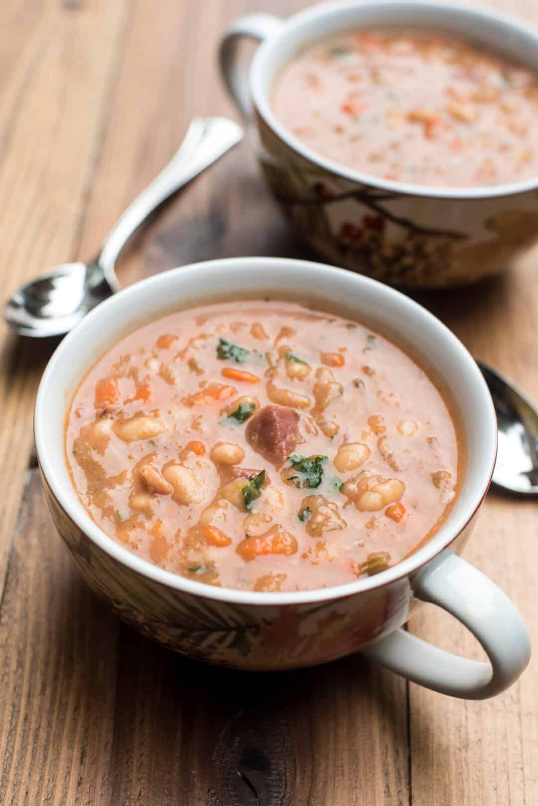 Two mugs filled with ham and bean soup on a wood cutting board.