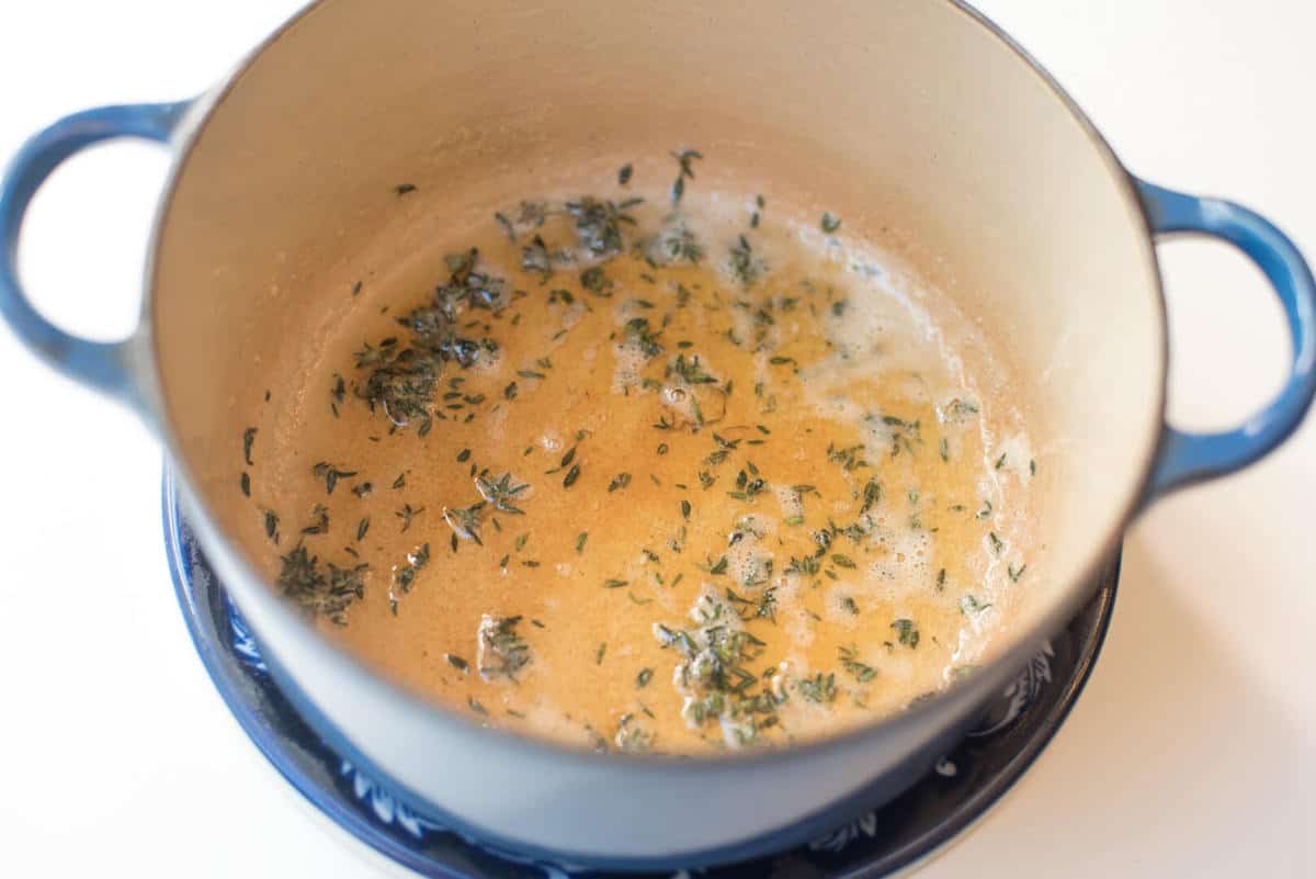 A blue Dutch Oven with melted butter and fresh thyme.