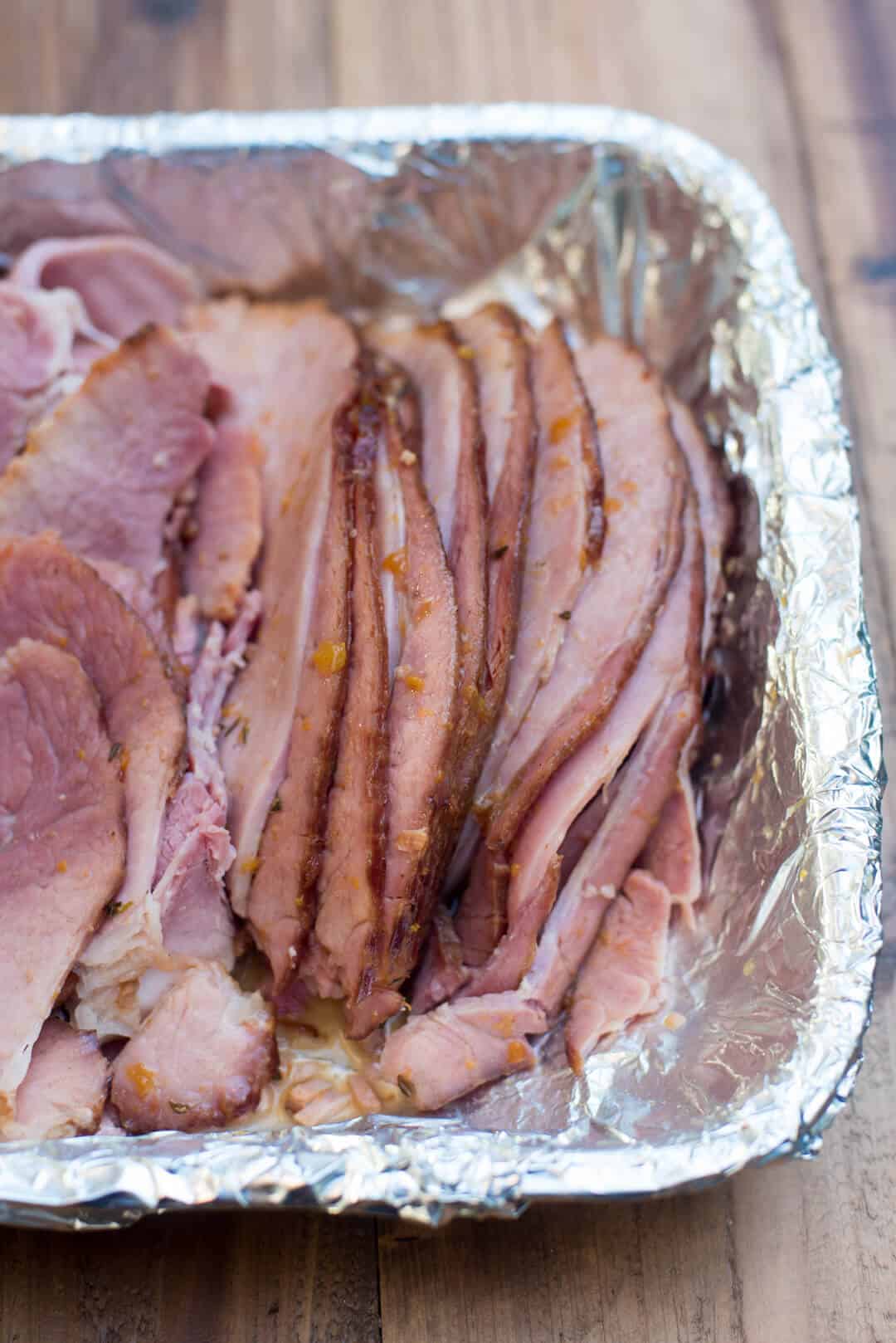 Sliced Slow Cooker Ham with Peach Thyme Glaze in a foil-lined dish.