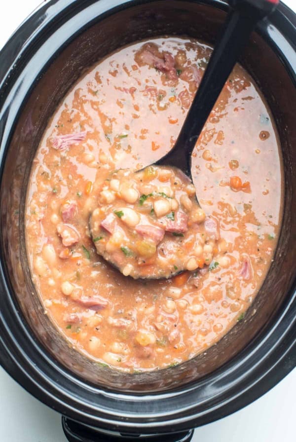 A ladle scoops Ham and Bean Soup from a slow cooker.