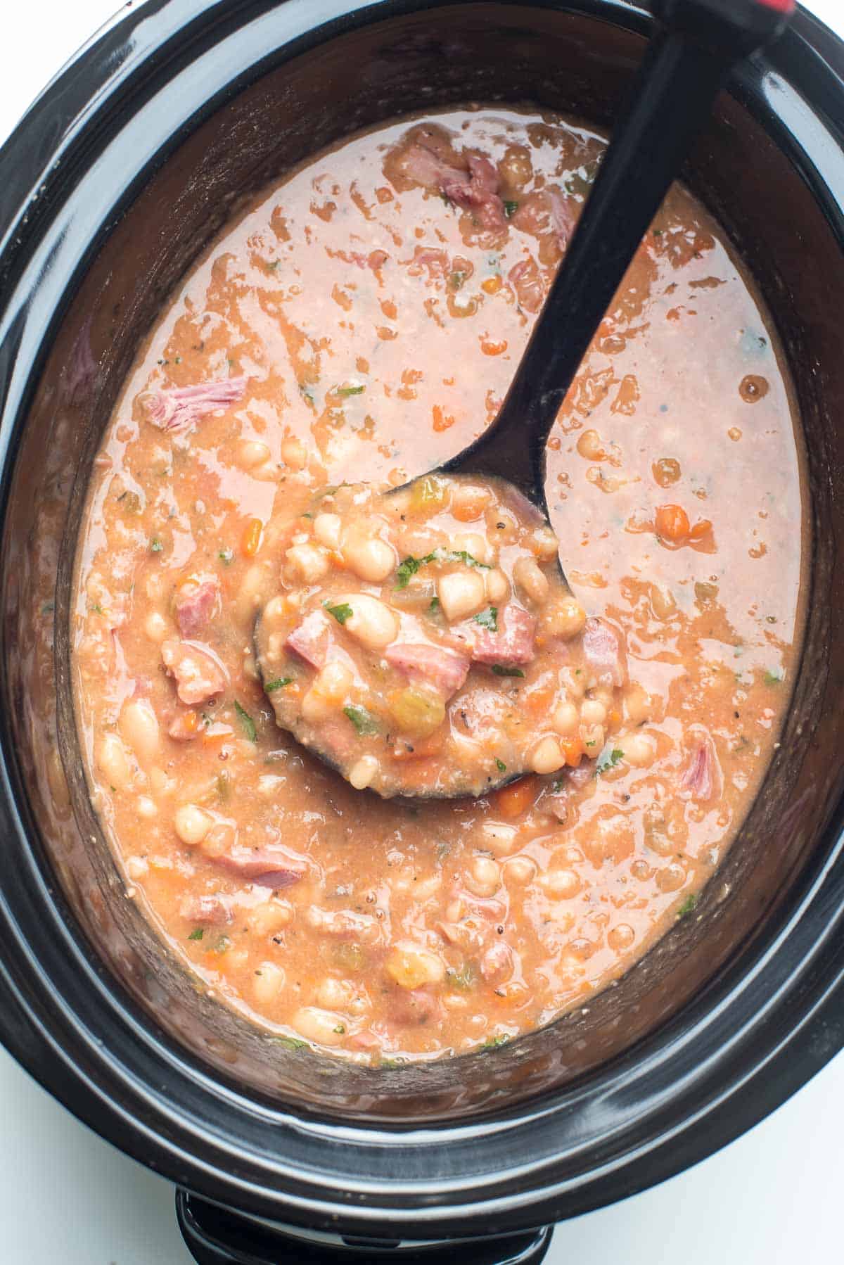 A ladle scoops Ham and Bean Soup from a slow cooker.