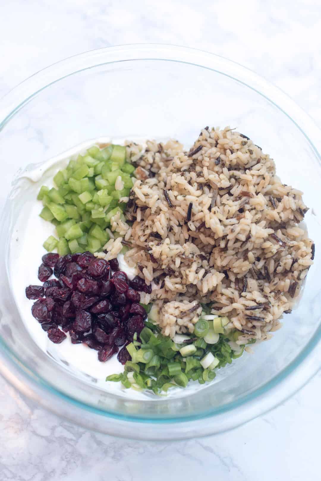 Wild rice, celery, craisins  and other ingredients in a glass bowl.