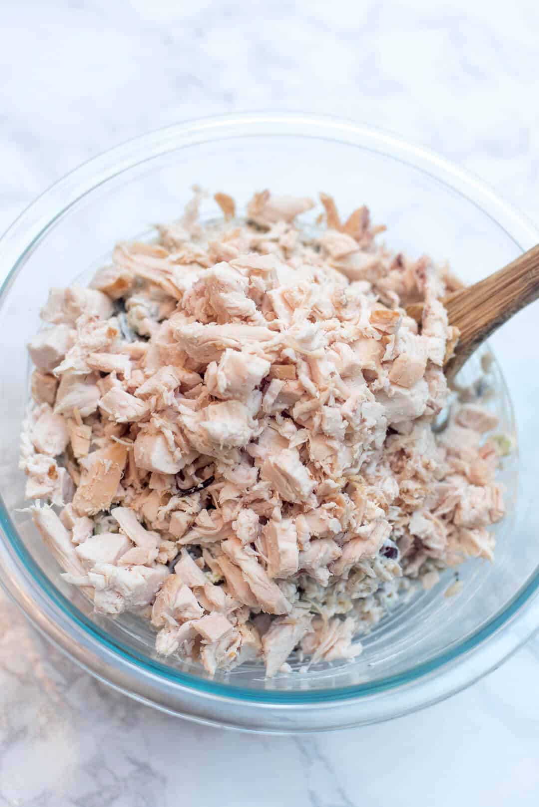 Chopped rotisserie chicken being stirred into a dressing mixture in a bowl.