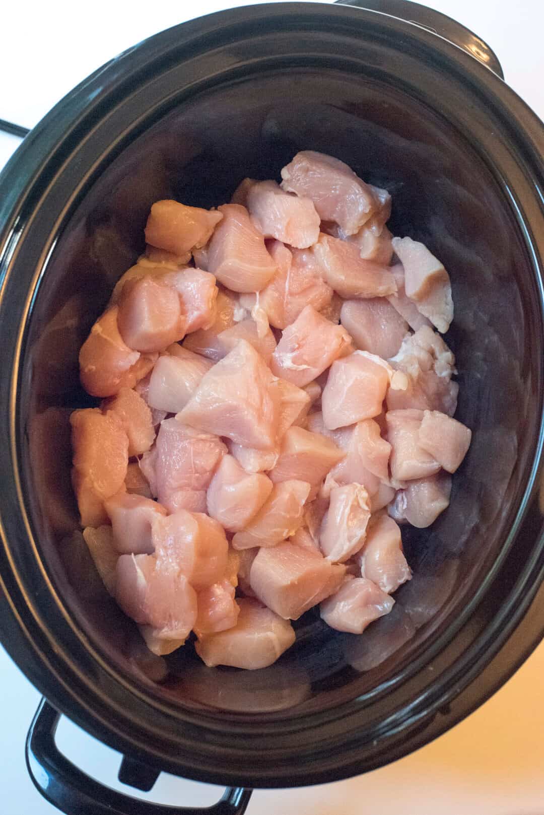 Raw, chopped chicken in a slow cooker.