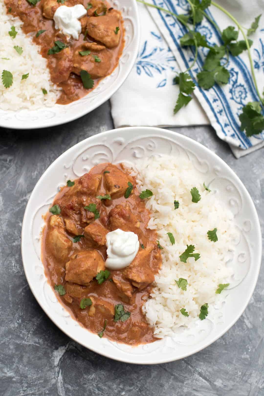 Chicken in sauce over rice in a white bowl topped with cilantro and Greek yogurt.