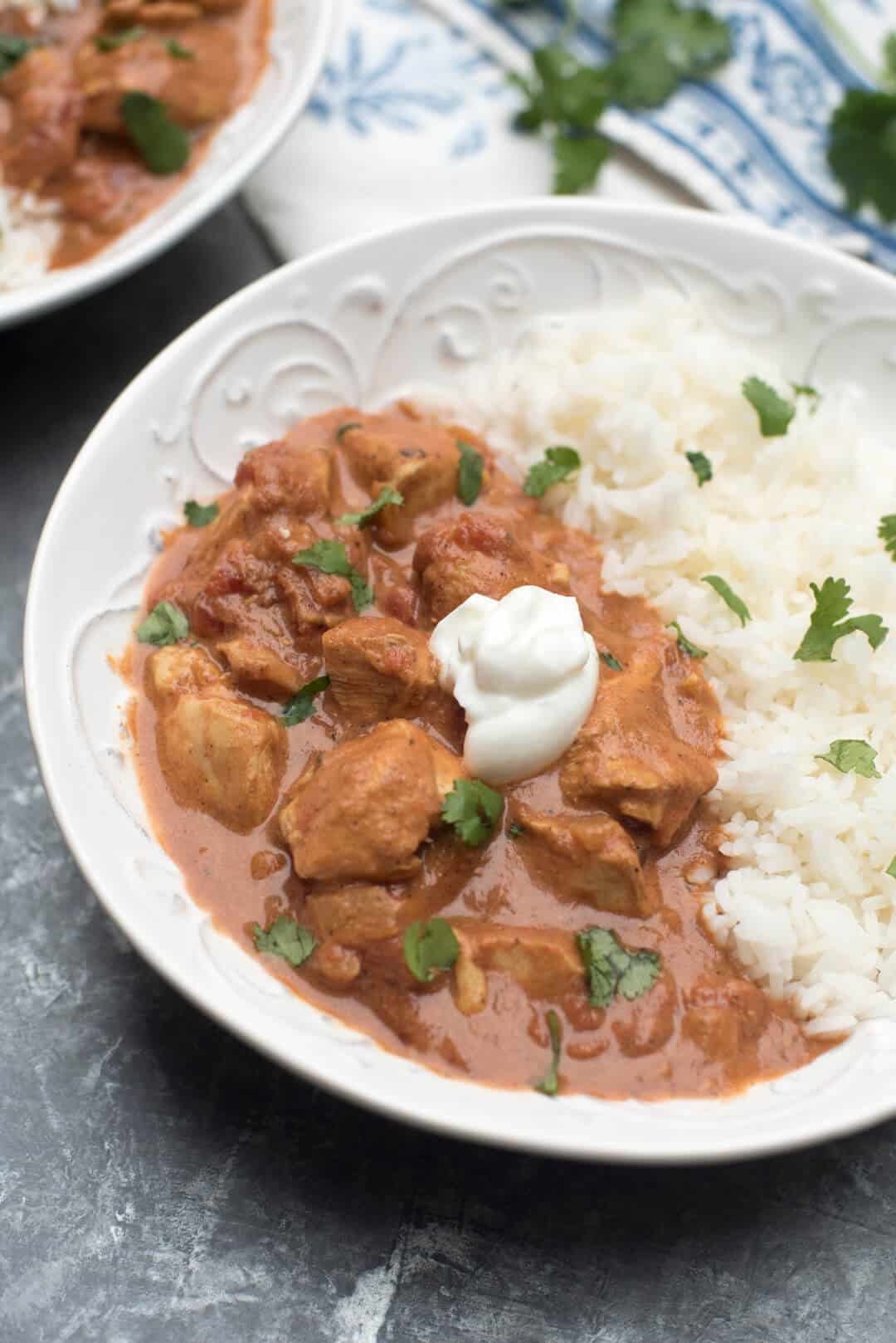 A bowl of Chicken Tikka Masala with rice topped with cilantro and Greek yogurt.