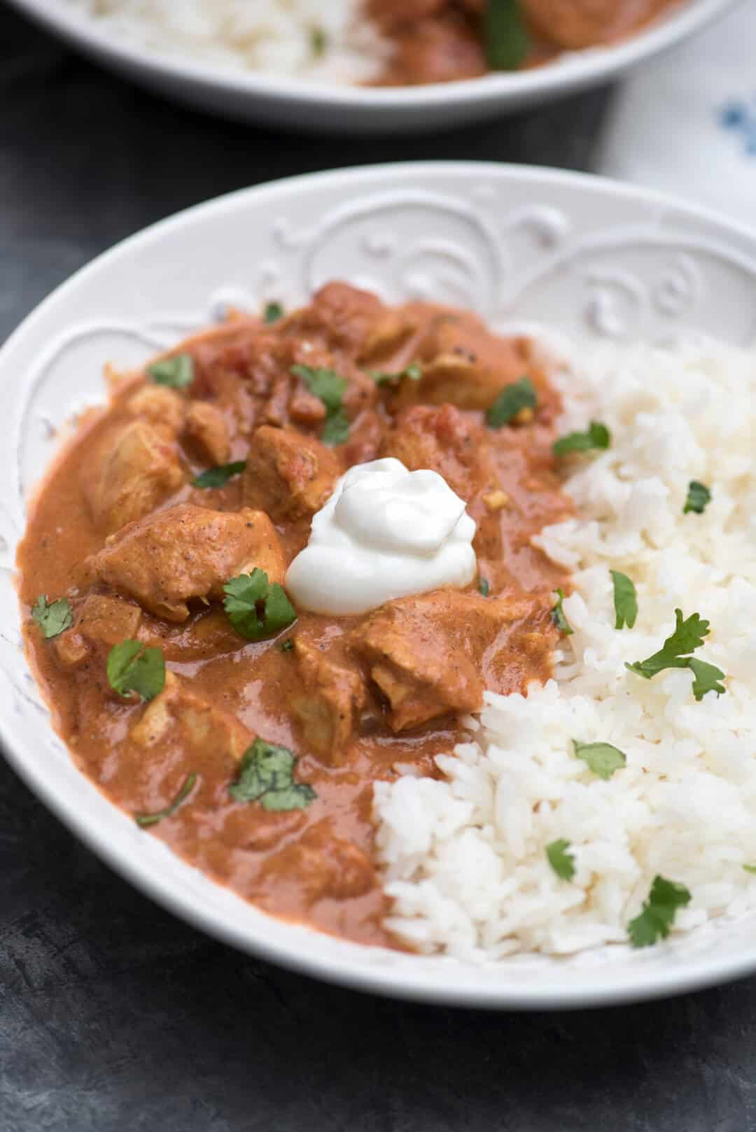 A closeup of Chicken Tikka Masala with white rice, cilantro and Greek yogurt in a bowl.