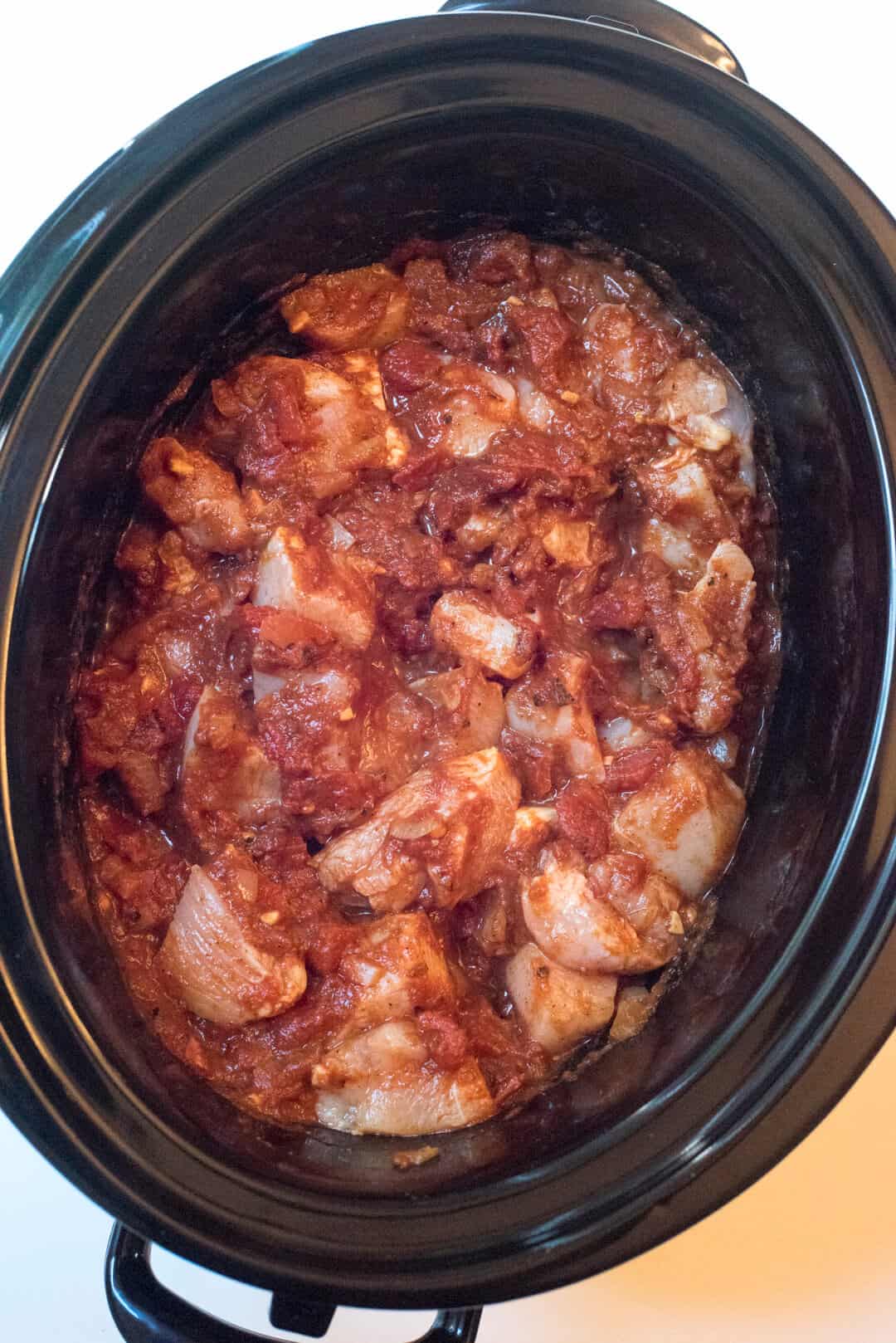 Raw chicken topped with sauce in a slow cooker.