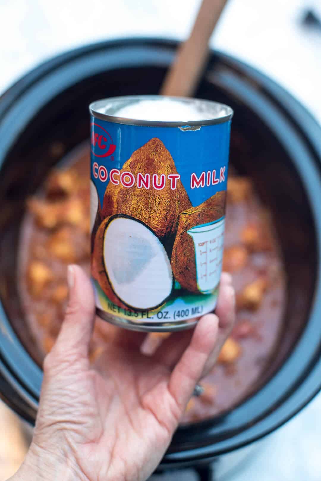 A can of coconut milk is held above a slow cooker.