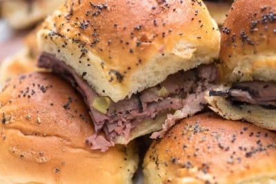 A close up of Italian Roast Beef Sliders stacked on a white plate.
