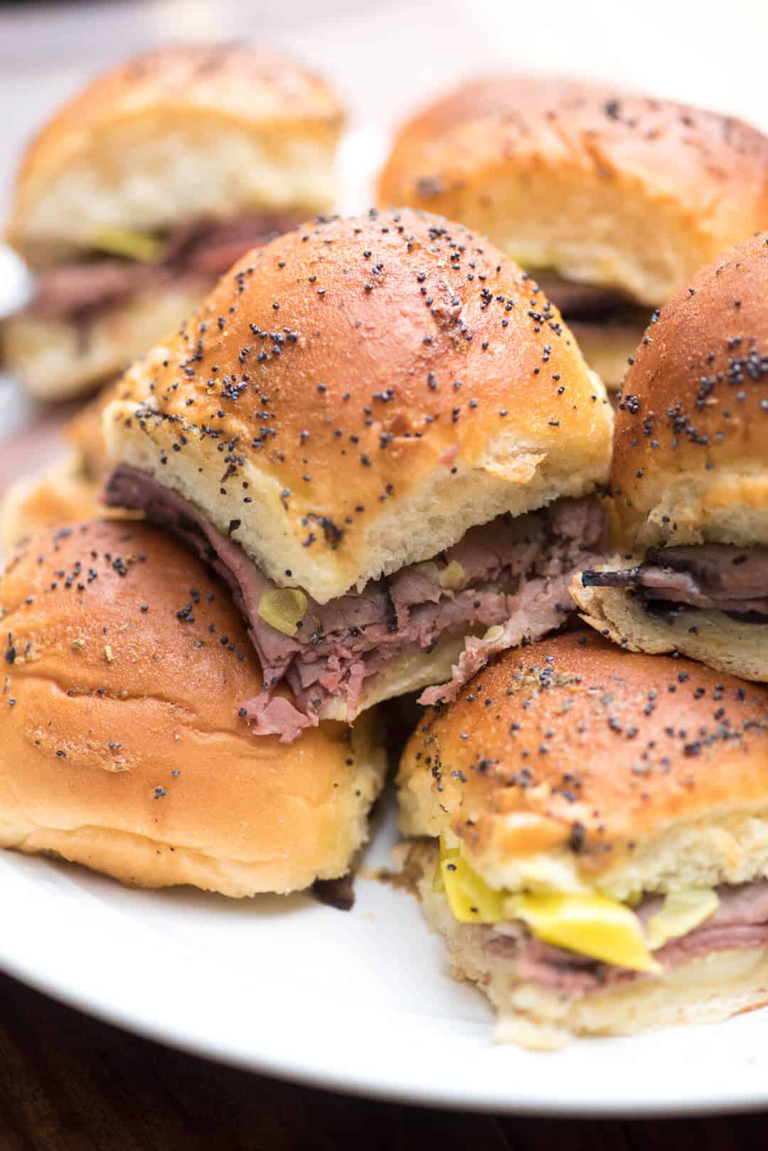 A pile of Italian Roast Beef Sliders on a white serving plate.