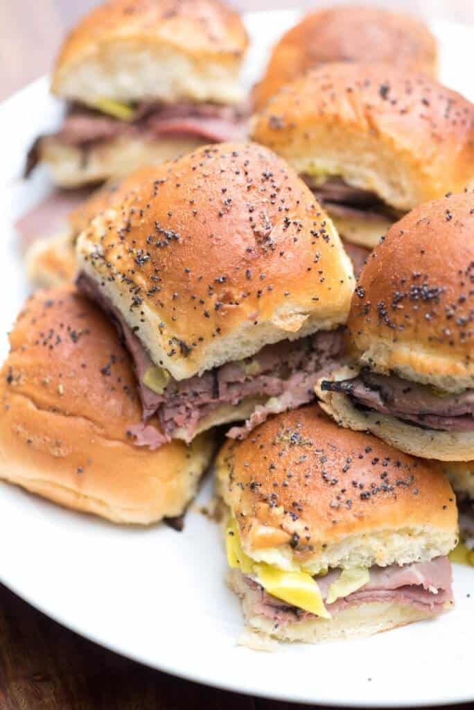 A pile of roast beef sliders on a white plate.
