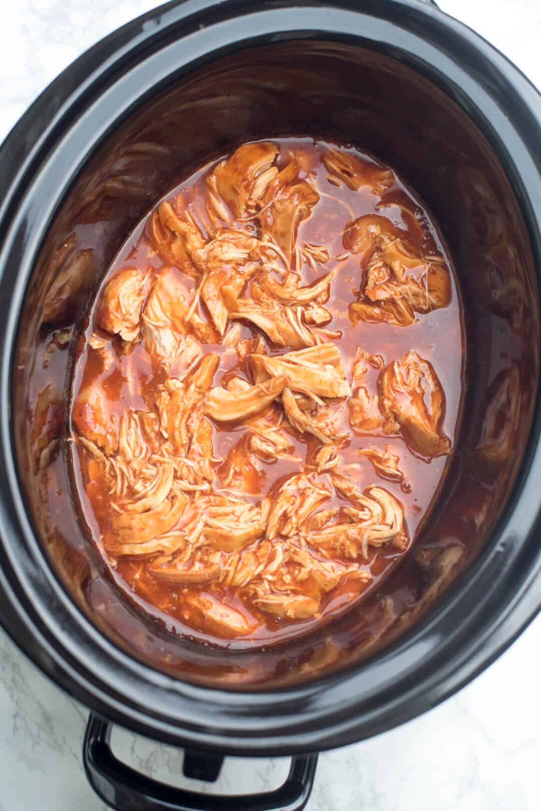 Cooked shredded chicken in sauce in a slow cooker.