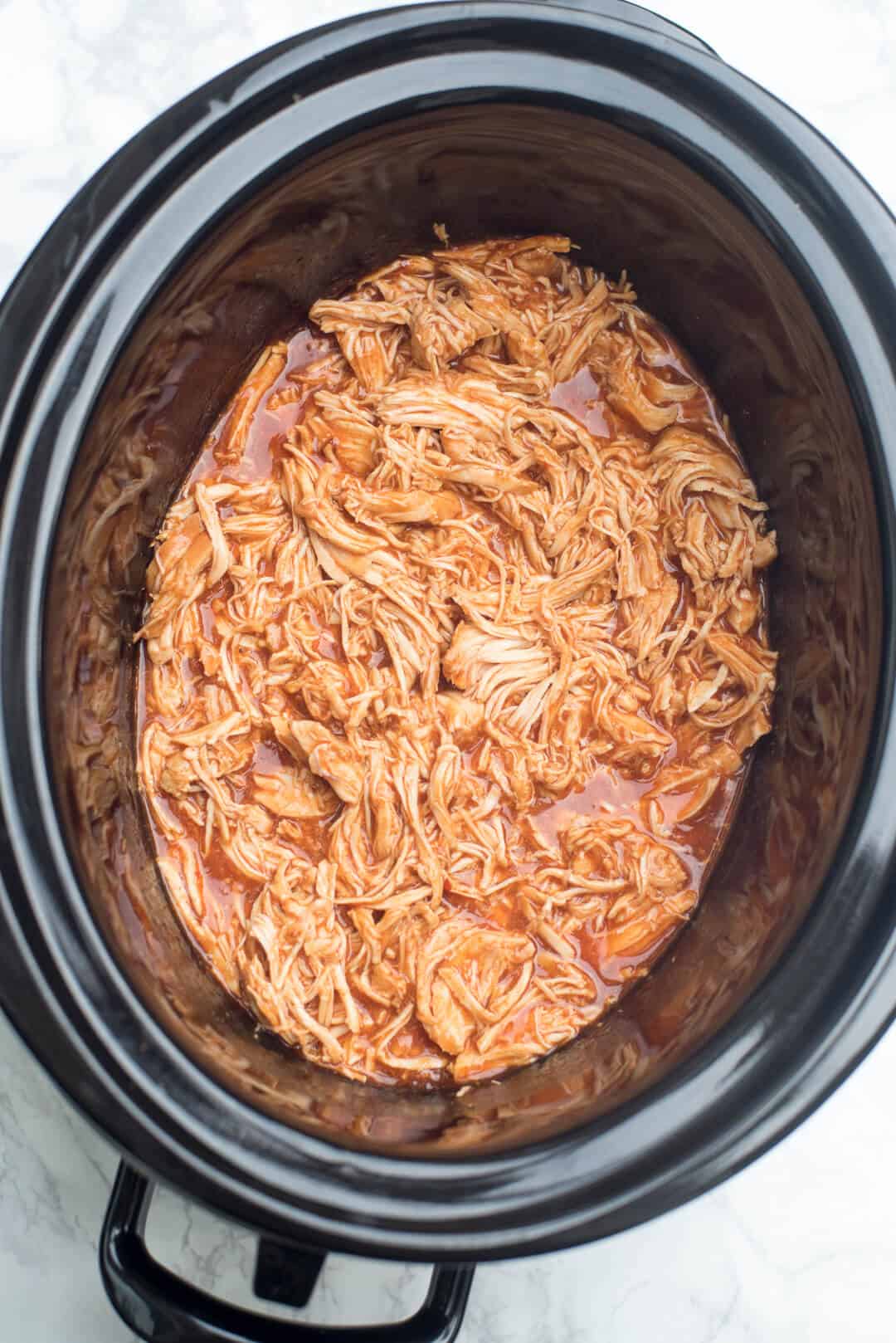 Cooked shredded chicken in BBQ and wing sauce in a slow cooker.
