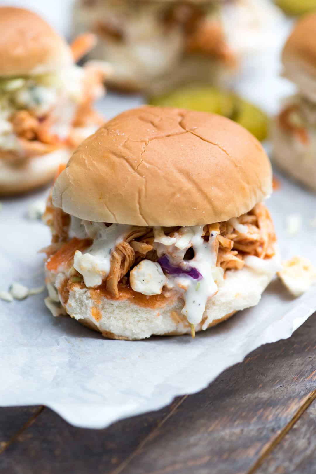 A closeup of a bbq chicken slider with Ranch dressing on parchment paper.