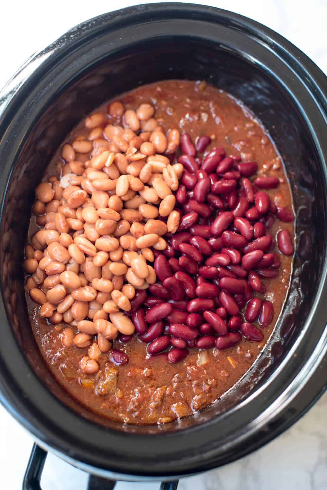 Pinto and kidney beans on top of a chili mixture in a slow cooker.