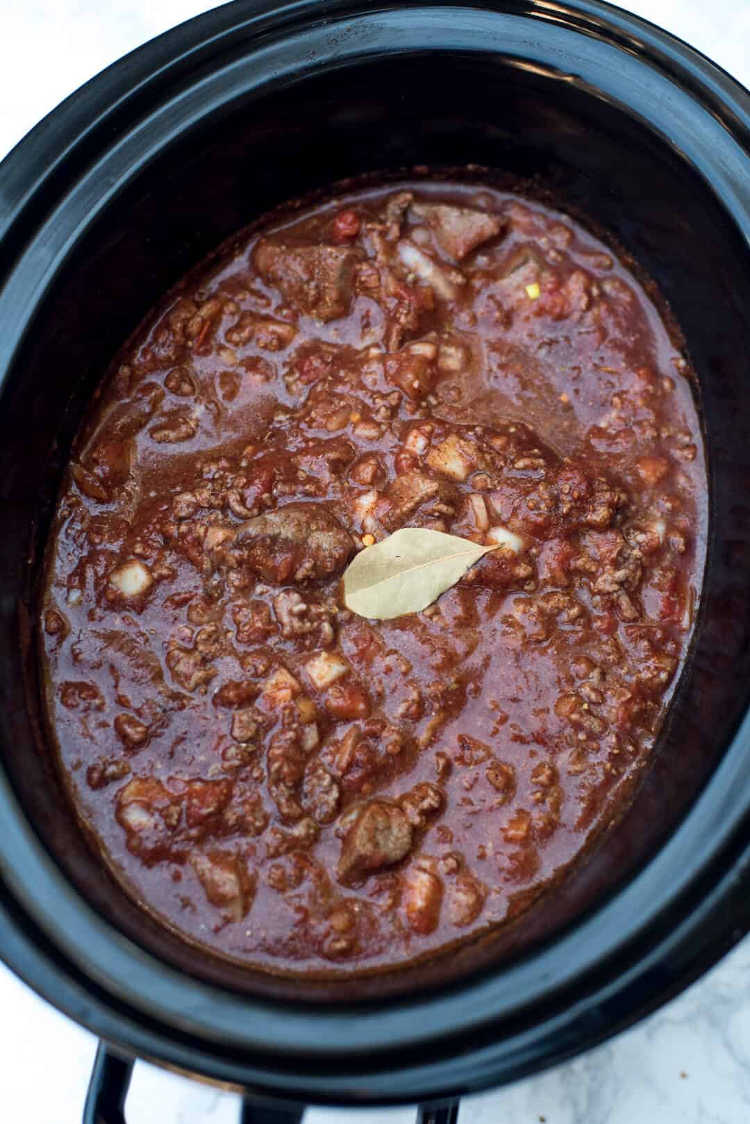 A bay leaf rests on top of a chili mixture in a slow cooker.