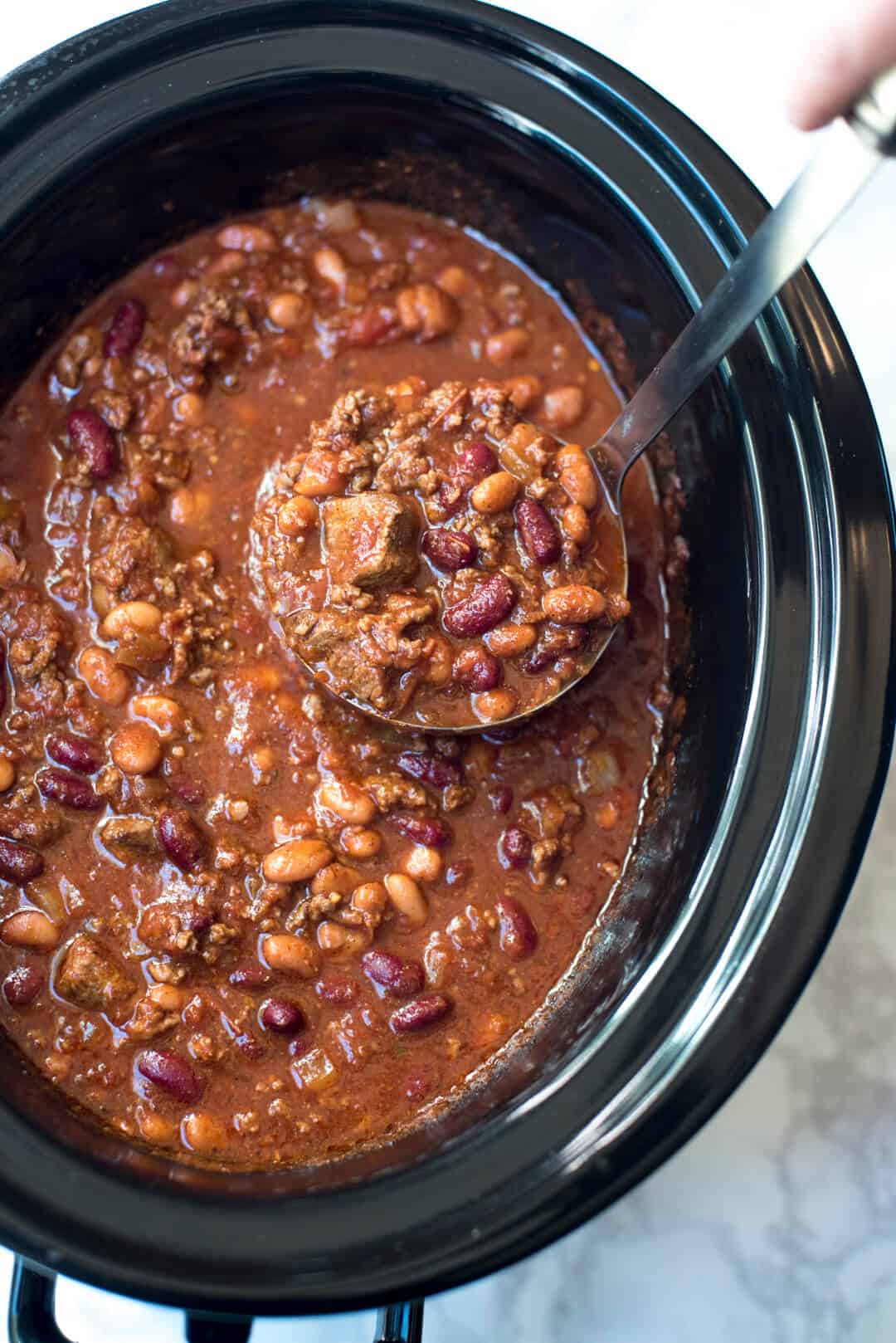 A top down shot of a ladle scooping up chili from a slow cooker.