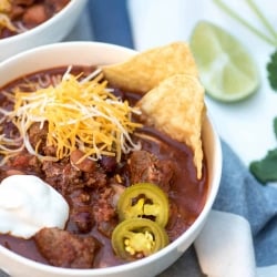 A bowl of chili topped shredded cheese, sour cream, jalapenos and tortilla chips.