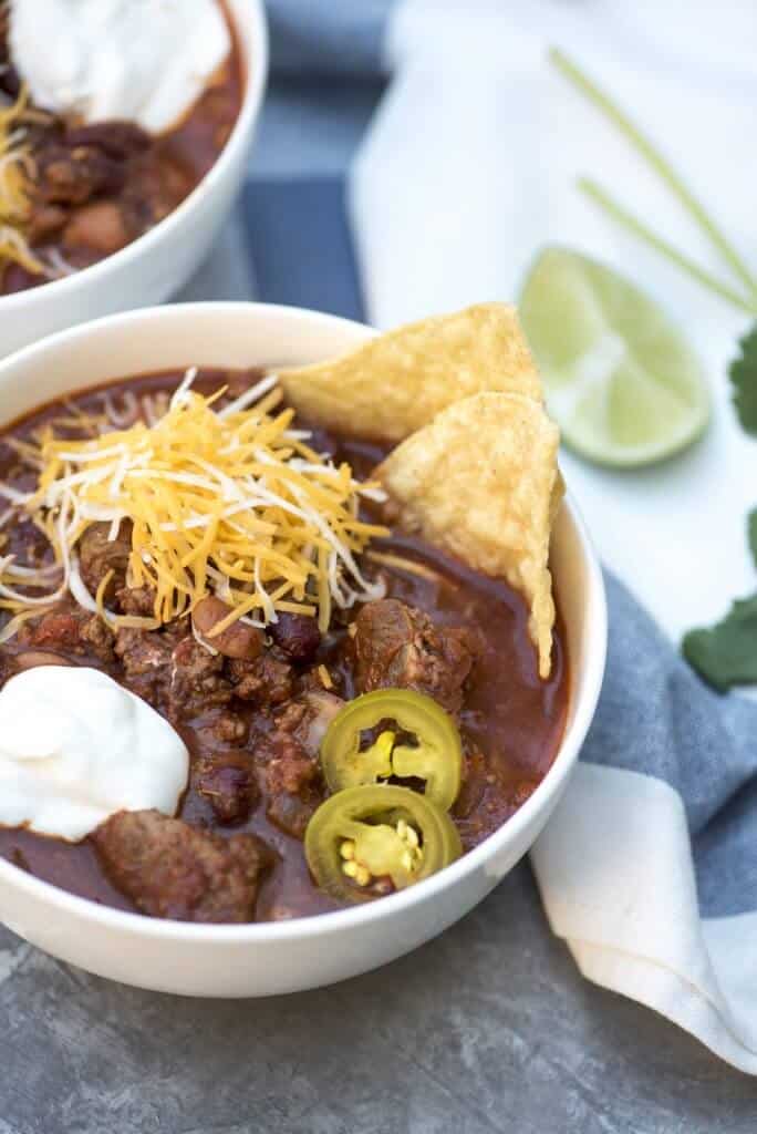 A bowl of chili topped shredded cheese, sour cream, jalapenos and tortilla chips.