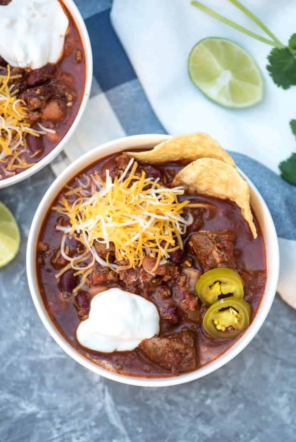 A bowl of chili topped shredded cheese, sour cream, jalapenos and tortilla chips.