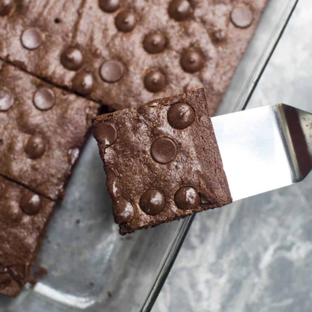 A spatula lifts a brownie from a baking dish.