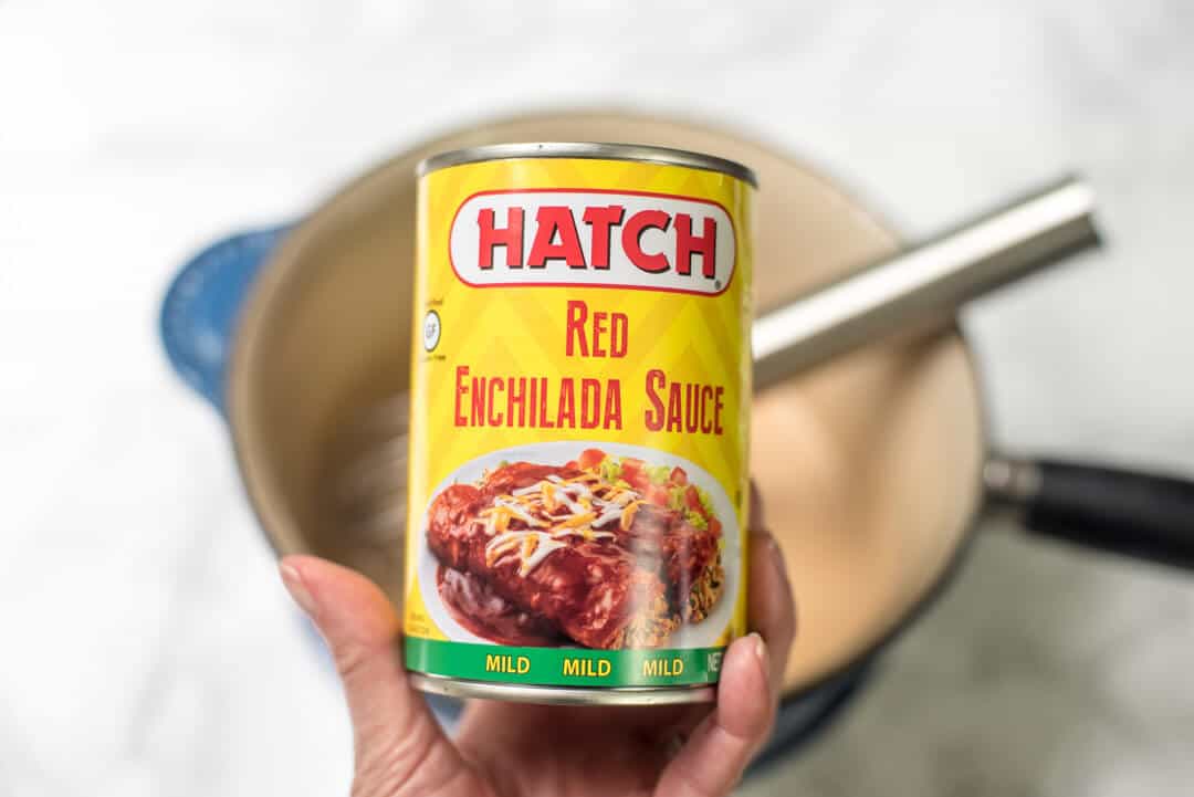 A hand holding a can of Hatch Red Enchilada Sauce.