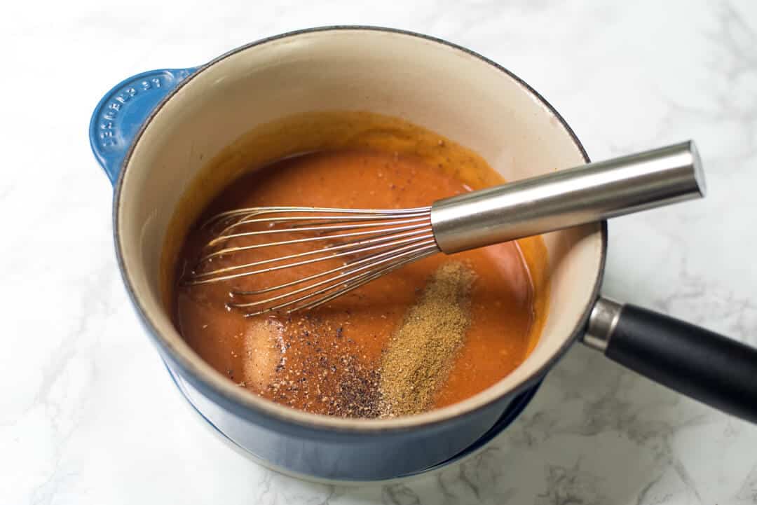 Enchilada sauce and spices in a saucepan with a whisk.