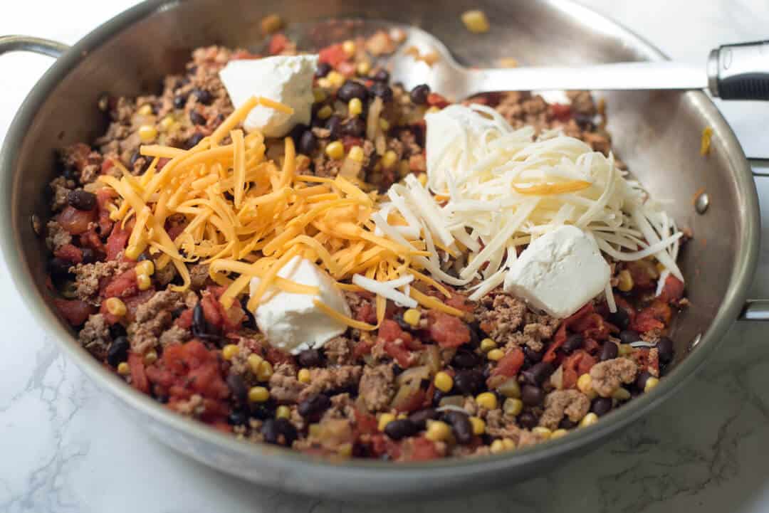 Cheddar, Jack, and cream cheese on top of a ground turkey and black bean mixture in a skillet.