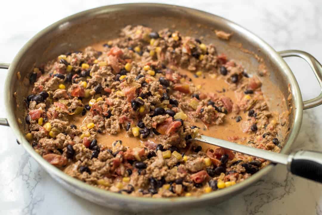 Turkey Black Bean Enchilada filling in a skillet with a spoon.